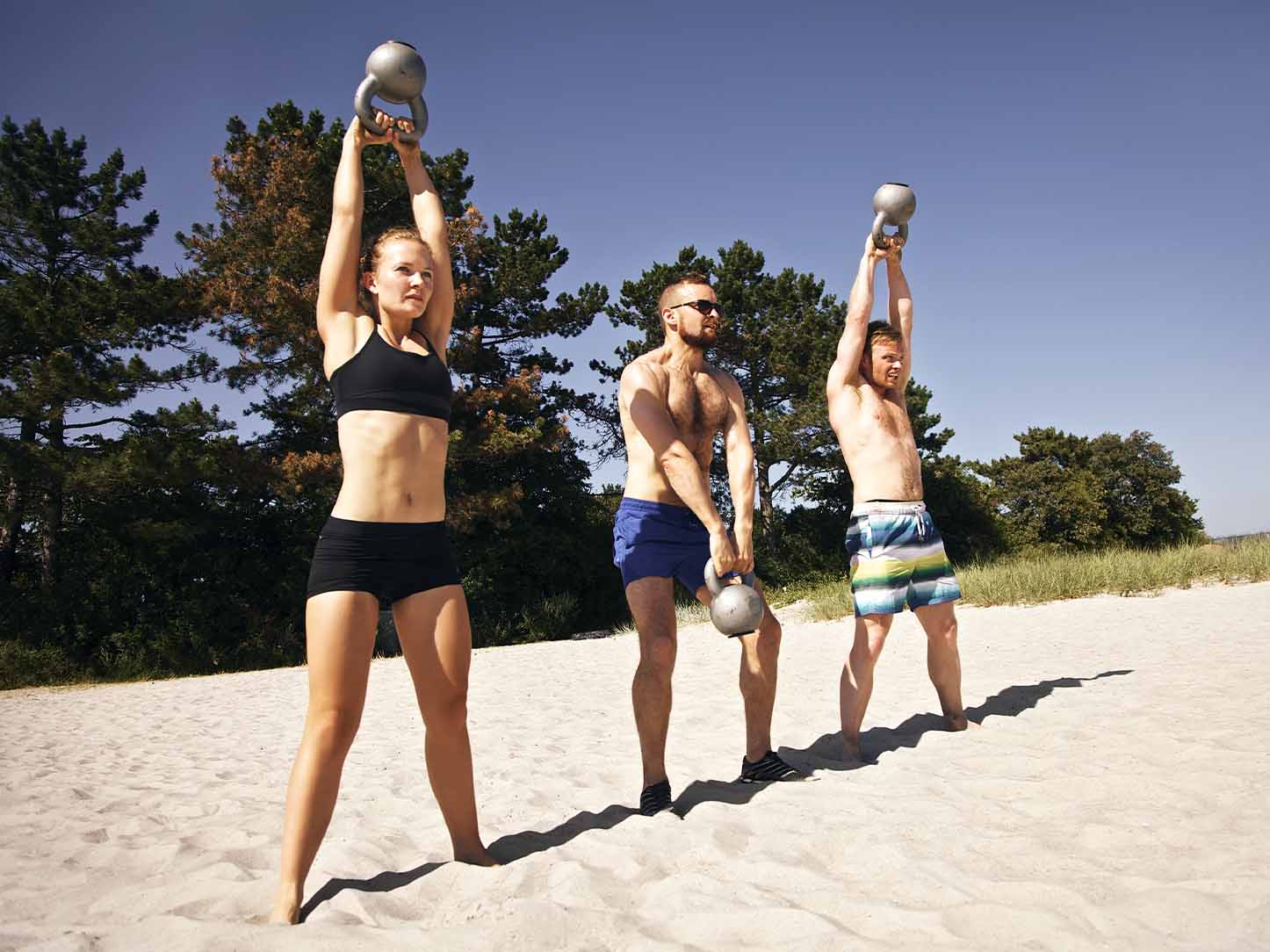Young people doing a kettle bell workout on a beach Young people doing a kettle bell workout on a beach